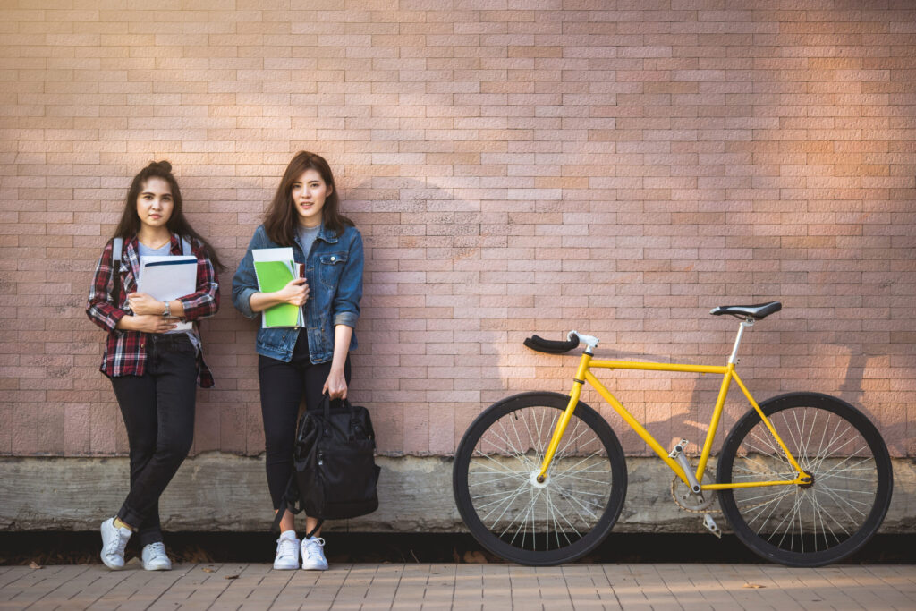 Two,asian,young,student,holding,book,standing,outdoor,near,bicycle